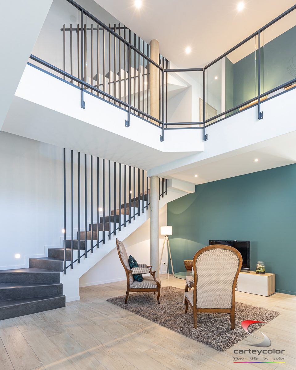 Duplex lumineux avec escalier, garde-corps noir et mur bleu canard